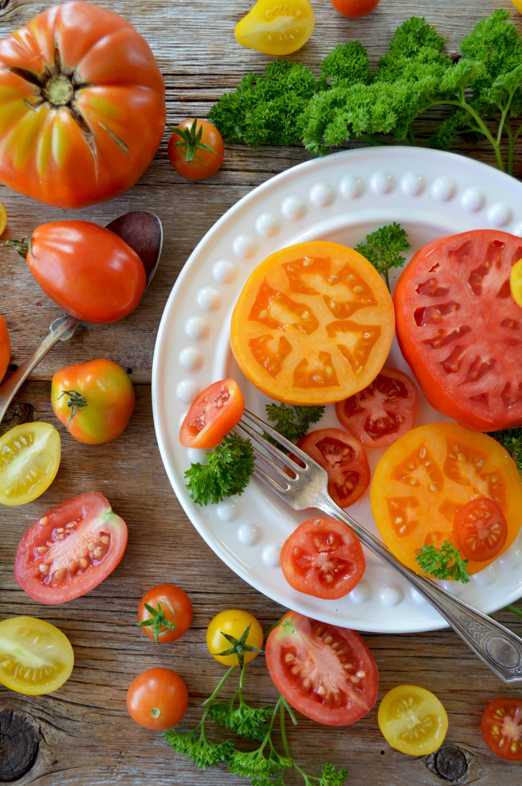 a white plate with sliced and whole tomatoes of various sizes and colors